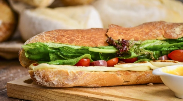 Image of a sandwich with spinach, cheese, and tomatoes, between a sliced flakey french roll.